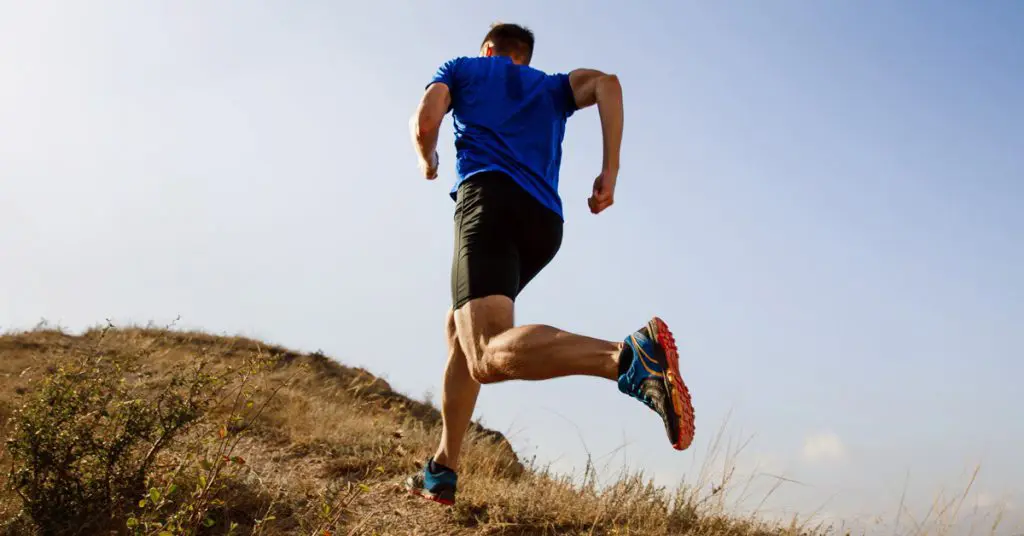 A man running up a hill in shorts, a shirt, and joggers.