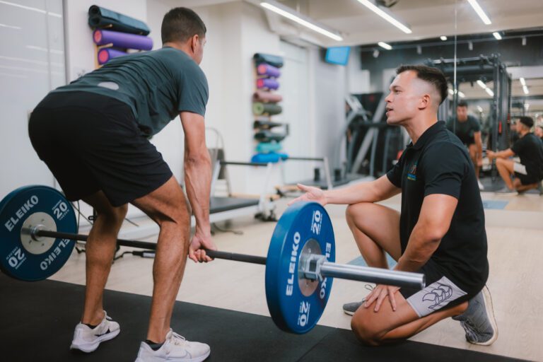 A personal trainer helping a man lift weight with proper form and technique.